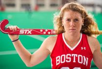 Portrait of Ally Hammel, Boston University Terriers field hockey NFHCA All-American, wearing her BU jersey and holding her stick on her shoulders.