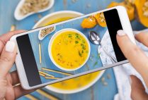 Woman taking photo of fall spicy pumpkin soup with herbs, croutons and sunflower seeds. Trendy instagram photo shot. Top view, flat lay style. Copy space
