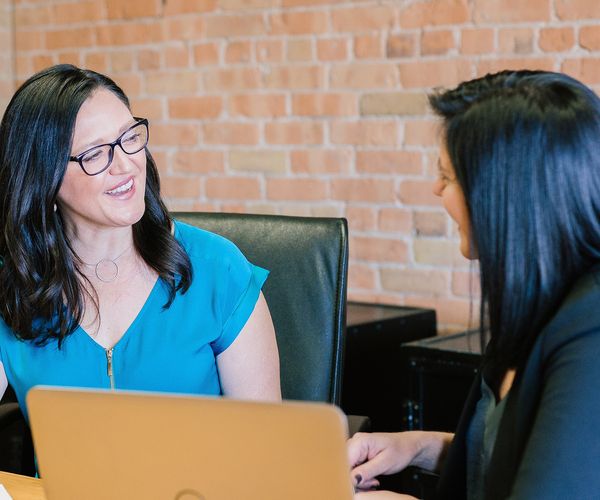 Two women face each other at a table with a laptop in front of them