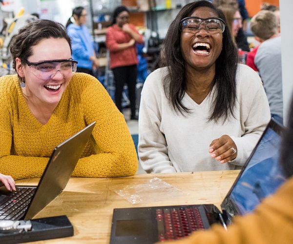 Female students smiling in a classroom wearing safety glasses