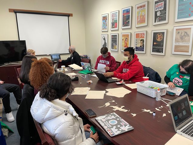 Students sit around a conference table with paper bird cutouts.