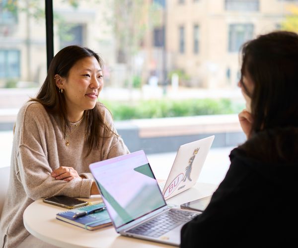 Photo of two students sitting at a table working together on laptops.