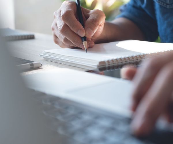 Photo of person's hands as they use a laptop and write notes