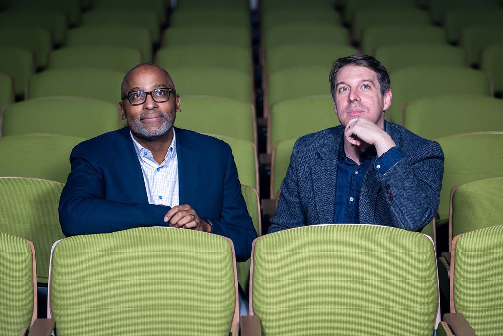 Film scholars and aficionados Harvey Young, dean of the College of Fine Arts (left), and Jonathan Foltz, a College of Arts & Sciences assistant professor of English and program director of its Cinema & Media Studies program, looking up at a film screen while sitting in an empty theatre with bright green seats.