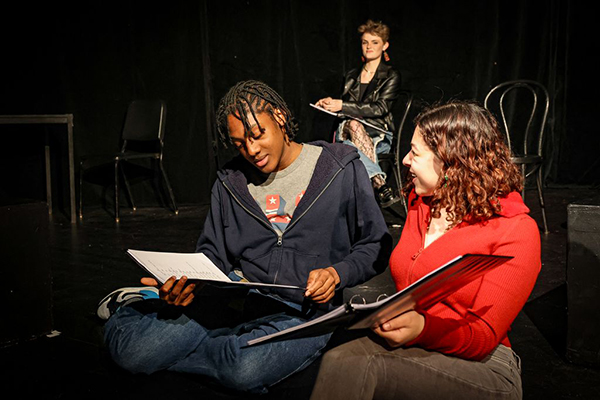Two acting students reading scripts in a black box theatre