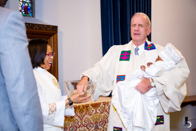 Pastor baptizes an infant while a second pastor assists