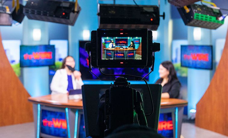 Look from behind the camera on set of butv10 news program the wire. News presenters at the anchor desk in the background.