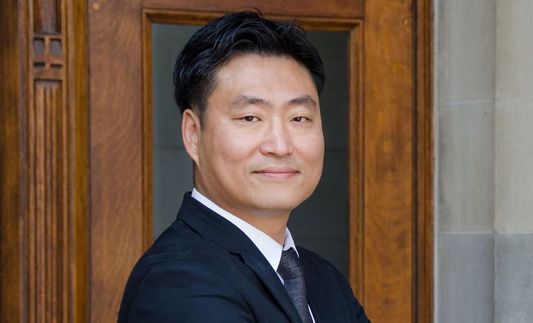 Sun Un Yang poses in dark suit with his arms crossed.