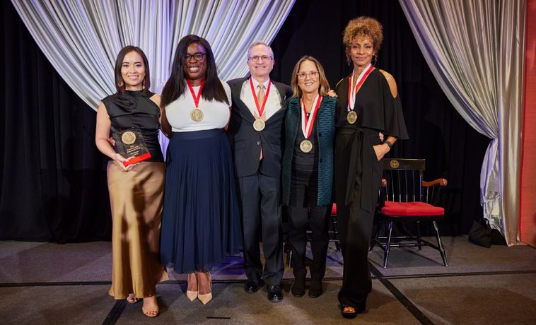 Four women and one man with gold medals stand on a stage.