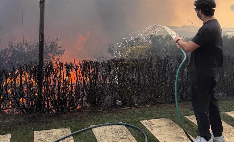 Young man from behind dousing a wildfire with a hose.