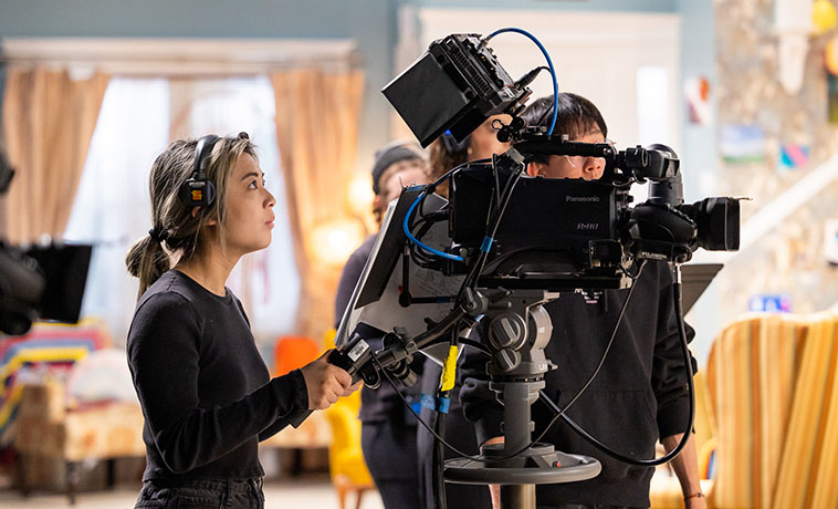 Young woman operating camera on set of Art House television sitcom.