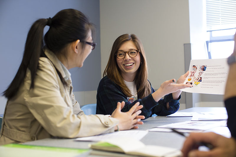 Two young women seated at table while reviewing copy.