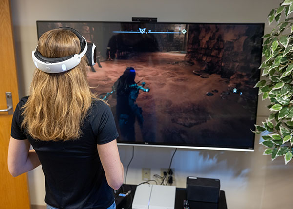 Woman wearing a headset while playing a video game on a large monitor.