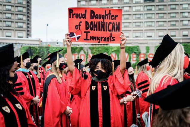 A graduating student holds a sign above her head that says 'Proud Daughter of DOMINICAN Immigrants' during the BU Commencement ceremony for advanced degrees.