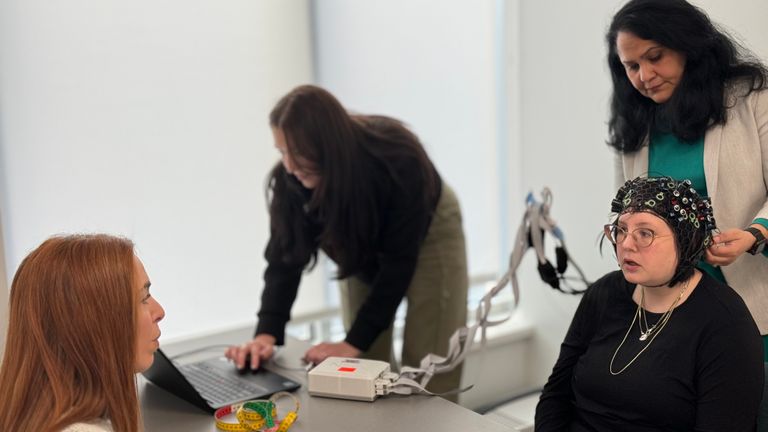 three people in a lab; one is wearing neural headgear