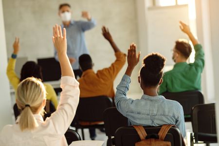 College students raising their hands to answer a question in a classroom