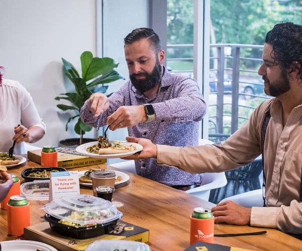 Group of 4 faculty members sharing a meal around a wooden table.
