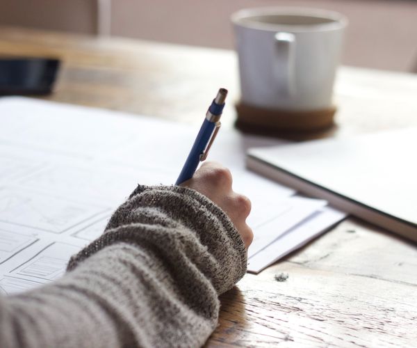 Person writing with pen on desk