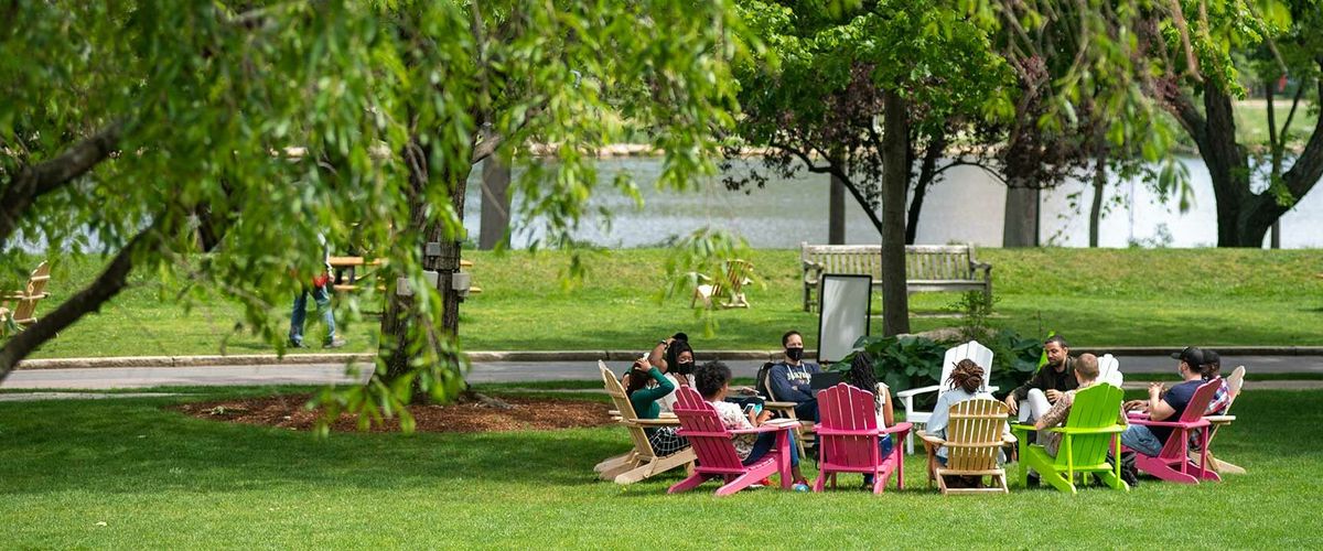 Photo of a group of students sitting on colorful chairs outdoors in a grassy park