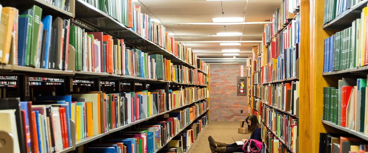 student sitting on floor of library reading