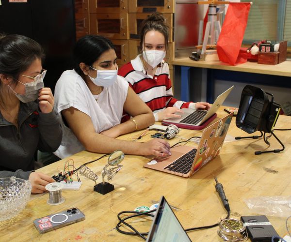 a close up of one table from the Lutron Lighting Ardiuno and Soldering workshop, a group of 3 students clustered around 2 laptops