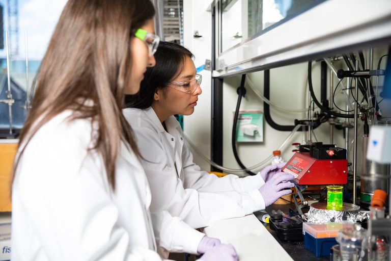 Two College of Engineering students wearing safety glasses while working with polymeric nanoparticles