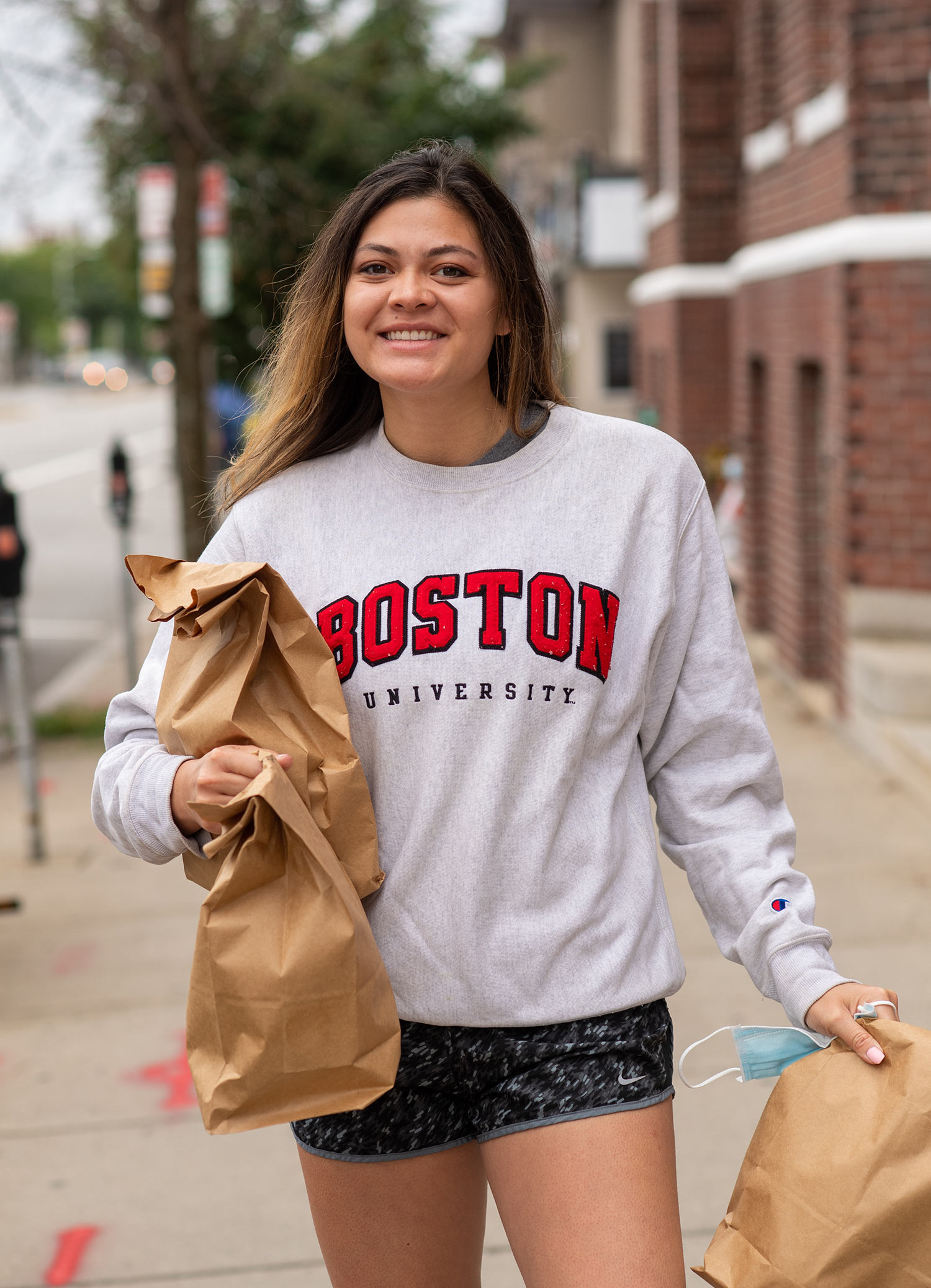 Photo of Lizy Flagg (ENG’20) in a Boston University sweatshirt during a volunteer shift for Rescuing Leftover Cuisine. She holds three brown paper bags.