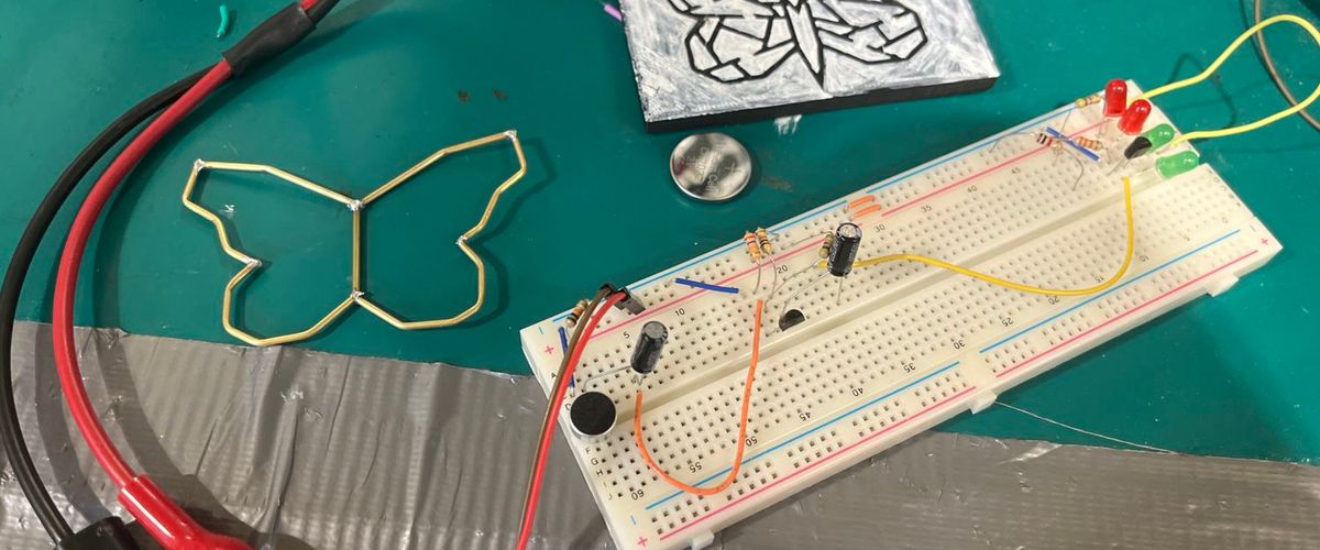 red and black wires connecting from a power supply to a breadboard with a variety of components. There is also a wire butterfly and a print of a more detailed line art butterfly