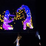 Two students act in front of a projected screen that displays computer generated blue and purple shadows of the actors that replicate their real life motions