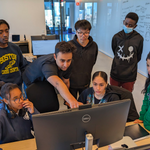 A group of software engineering students gather around a computer.