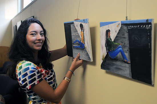 Giselle Blanco-Santana (CAS ’16) hangs her paintings at the Howard Thurman Center for Common Ground for the BU Arts Initiative forum for student art and dialogue, “Race, Identity & Art”. The student exhibit will begin on October 7 at 6 p.m. and will run through October 21. For this set of paintings, Blanco-Santana was inspired by her own experience as a Latino growing up in a predominantly African-American neighborhood. She says she never understood why Mexican and African-American cultures failed to find common grounds although people experienced “mirror situations,” which she illustrated with two girls sitting on opposite sides of a fence in the same poor neighborhood.