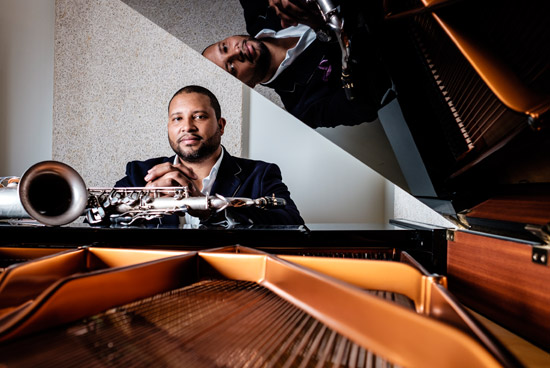 Jimmy Greene poses at the piano with saxophone