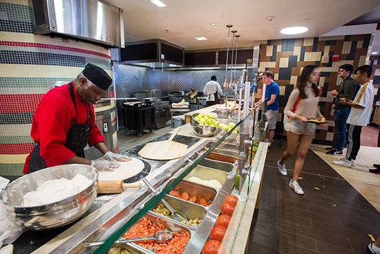 a chef prepares a pizza while students line up to get food