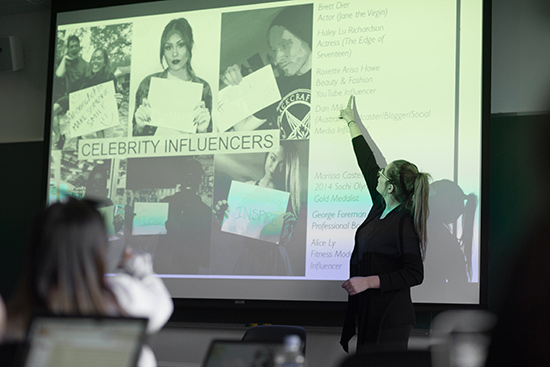 Elle Hvozdovic (COM’17) stands in front of a projector screen