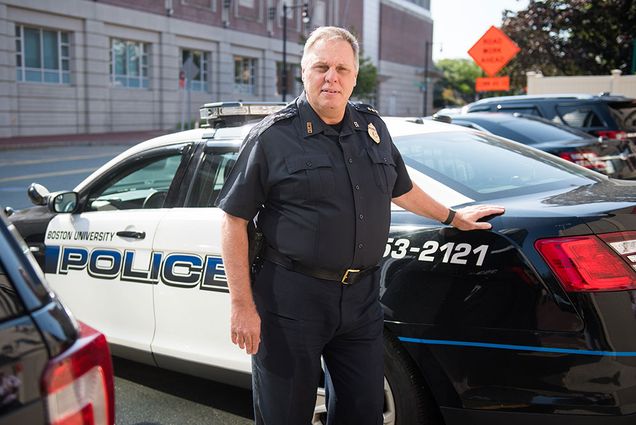 Robert Molloy, a member of the BU Police Department for three decades, leans on his BUPD car for a photo