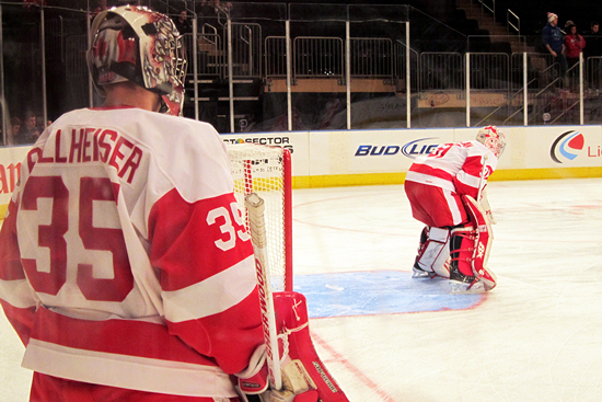Two Boston University Hockey players stand to defend the goal.