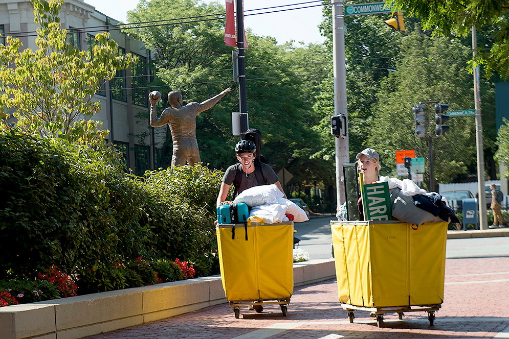 Two students rolling their yellow moving carts down a brick campus walkway