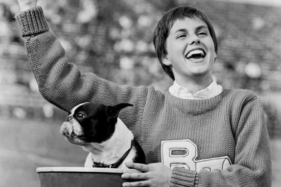A cheerleader holds Rhett the Terrier, BU mascot, during a football game in 1960
