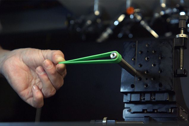 A hand pulls back on a rubber band getting ready to "shoot" it from a lab machine as part of an experiment researching physics of shooting rubber bands and plucking guitar strings