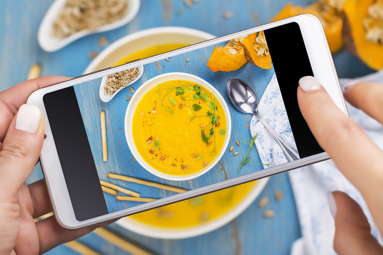 Woman taking photo of fall spicy pumpkin soup with herbs, croutons and sunflower seeds. Trendy instagram photo shot. Top view, flat lay style. Copy space