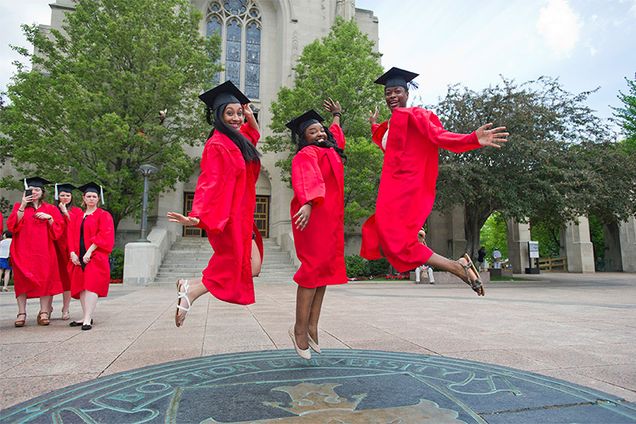 Three Boston University graduating students jump on the BU Seal symbol on Marsh Plaza on Commencement Sunday.