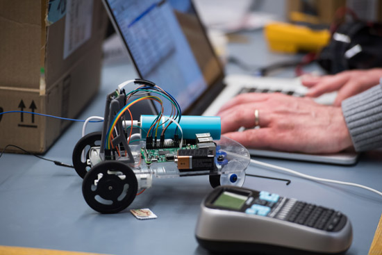someone types code into a computer with a small robot next to them