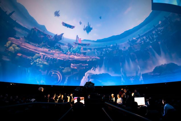 View from within the Omni Theatre in Boston's Museum of Science. A preview of gamers on their laptops in the theatre playing overwatch live on the dome screen above them.