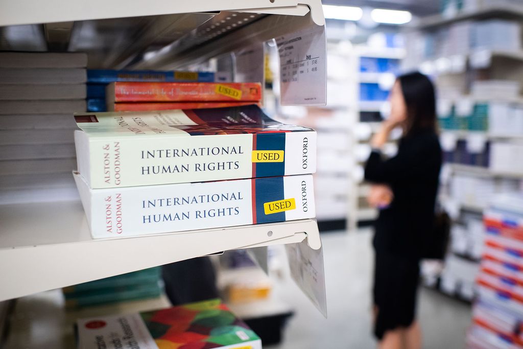 Two used copies of an International Human Rights textbook on a shelf with a customer browsing textbooks in the background