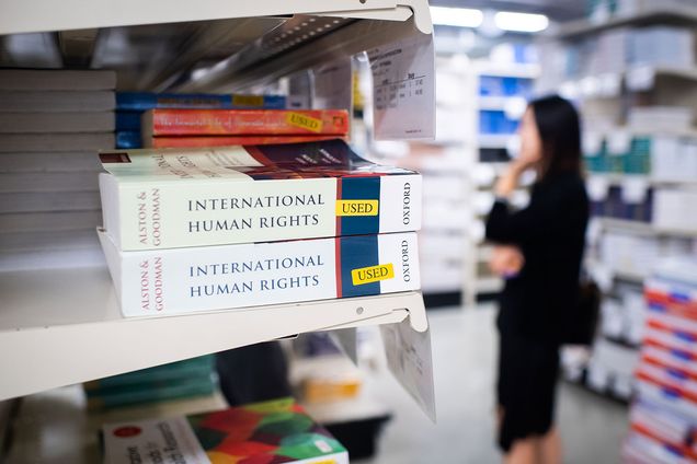 Two used copies of an International Human Rights textbook on a shelf with a customer browsing textbooks in the background