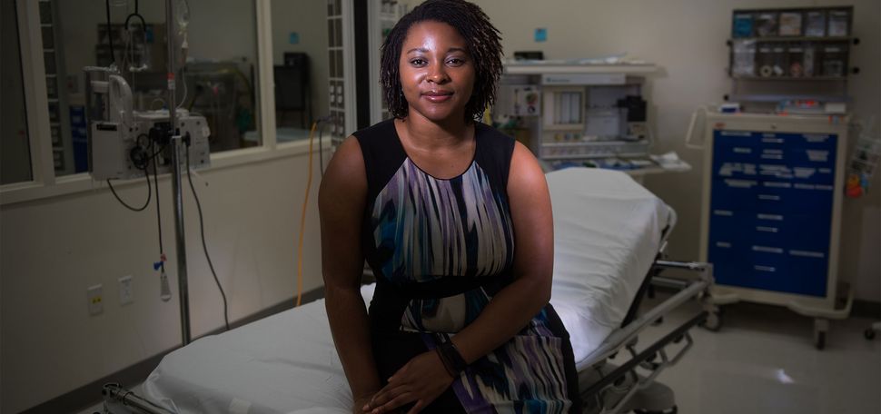 Dr. Tejumola Adegoke, and OBGYN at Boston Medical Center, sitting on a gurney in an operating room.