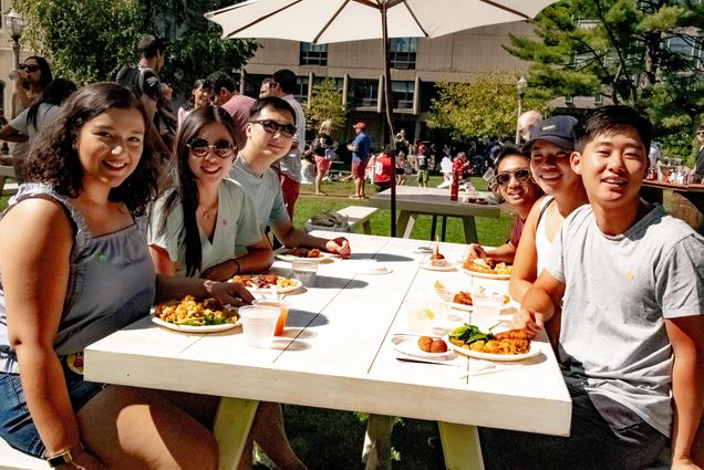Boston University alumni at a picnic table pose for a photo at the Alumni Weekend picnic on BU Beach