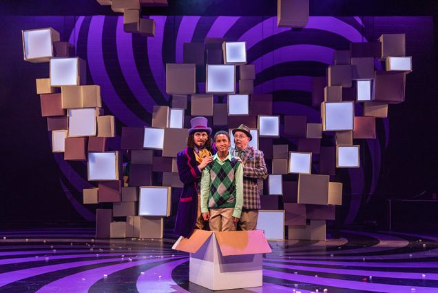 Ricky Holguin (left) as Willy Wonka, Jamie Leslie as Charlie Bucket, and Neil A. Casey as Grandpa Joe in Wheelock Family Theatre’s production of Roald Dahl’s Willy Wonka