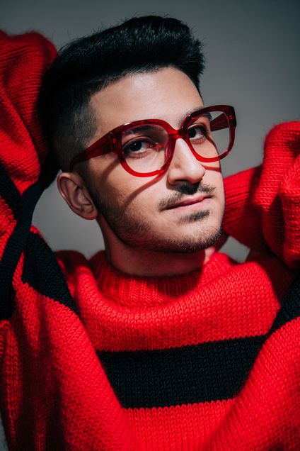 Tareq Alkhudari (COM’20) poses wearing red-frame glasses and a matching red sweater