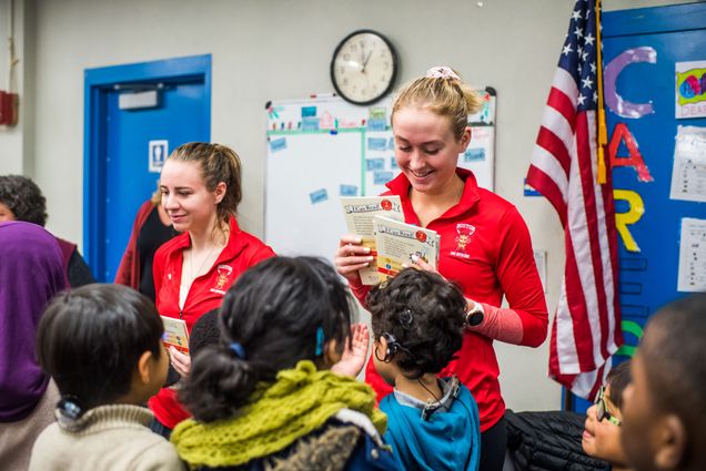 Members of the Women's Rowing team including, Kate Horton (left) (CAS 19) and Grace Beery (CAS 21) hand out book to students at Horace Mann Elementary School on Friday, December 13, 2019.